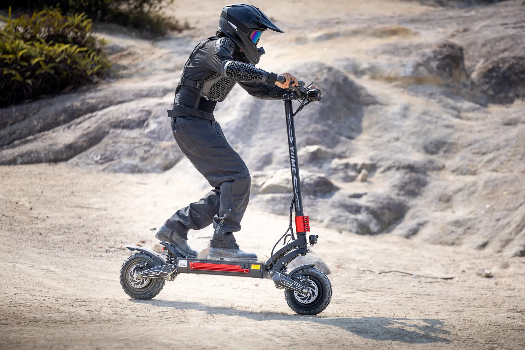 Rider in full protective gear on a YUME Raptor 2 electric scooter on rock